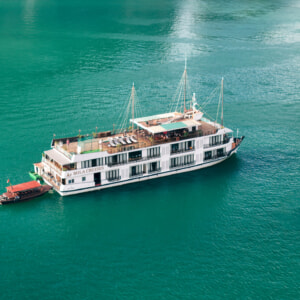Aerial view of a Mila Cruises vessel with a small tender boat on calm emerald water in Halong Bay